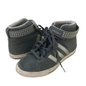 Adidas sneakers med nitar, blå/grå - Säljer ett par grå/blå sneakers från Adidas med silverfärgat nit spänne runt ankeln och klassiska ränder på sidan. Skorna har snörning och är tillverkade i mocka. Använda en gång!