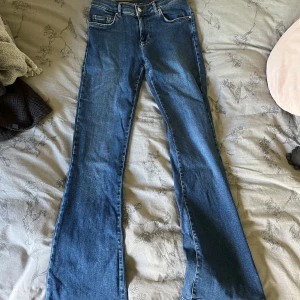 Blå low flare jeans - Säljer ett par blå jeans med låg midja och flare-ben. Klassisk femficksmodell med knapp och dragkedja framtill. Jeansen har en snygg passform som sitter tajt upptill och släpper ut vid benen. I midjan är den st S och i benen längd 31, de är knappt använda!
