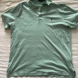 Turkos pikétröja från Ralph Lauren - Säljer en Turkos pikétröja från Ralph Lauren med klassisk krage och knappar framtill. Tröjan har korta ärmar och schysst logga på framsidan.  Storlek L men sitter som en M. Priset är ej hugget i sten, och diskuterade vid snabb affär💰. Skick 8/10, vid minsta fundering eller priförslag hör av dig!!