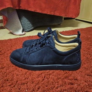 Mörkblå louboutins - Snygga mörkblå sneakers i mocka från louboutin med rund tå och platt sula. Låda ingår ej. Skorna har svarta snören och en kontrasterande orange sula undertill med louboutin-logga. Köparen står för frakten. Insidan är ljusbeige och de har en stilren, minimalistisk design.