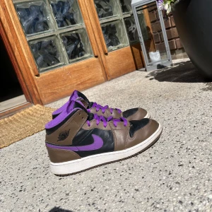 Nike Air Jordans i brunt och lila - Säljer ett par Nike Air Jordans med brun och svart bas, lila detaljer och snörning. Skorna har vit sula och klassisk hög modell. Perfekta för dig som vill sticka ut med färg och stil.