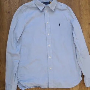 Ljusblå skjorta från Polo Ralph Lauren - En stilren skjorta från Ralph Laurén till ett bra pris. Bara använd fåtal gånger och säljs då den är för liten. storlek 170-175 hör gärna av er vid frågor