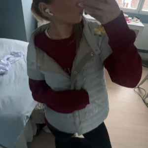 Glittrig silver dunväst från Herno - Säljer en glittrig silverfärgad dunväst från Herno. Västen har korta ärmar,  och stängs med knappar framtill. Perfekt för att ge din outfit lite extra shine och värme. 