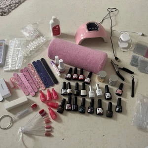 Stort nagelkit med lampa och gel-lack och tillbehör - Nagelkit med flera gel-lack i olika färger, top coat, base coat, glitter i burk (guld & silver), nagelfilar, nagelklämmor, nagelborste, UV-lampa i rosa, nagelverktyg och dekorstenar. Perfekt för kreativa nageldesigner hemma. Många är ny 