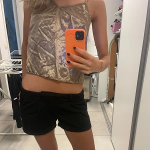 Beige glansig croppad linnetopp - Säljer en beige glansig croppad linnetopp med tunna axelband och asymmetriska sömdetaljer. Perfekt för sommaren och enkel att styla till olika outfits. Säljer också shortsen se annan artikel. Toppen saknar en knapp men det är lätt att fixa 