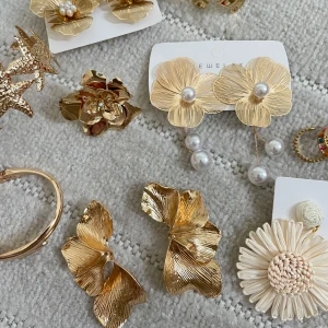 Stora guldiga blomörhängen med pärlor - Säljer ett par stora, blommiga örhängen i guldfärgad metall med fina detaljer och små vita pärlor i mitten. Perfekta för att ge din outfit en extra touch av elegans och stil.