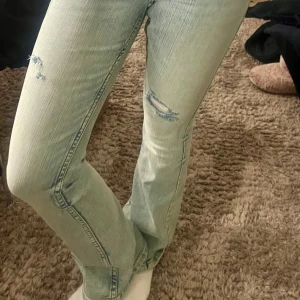 Ljusblå bootcut jeans med slitningar - Säljer ett par ljusblå jeans med bootcut-modell och slitna detaljer på låret och knät. Jeansen har klassisk femficksdesign och är i ett mjukt denimtyg. Perfekta för dig som gillar en avslappnad och trendig stil. Storlek 164, men sitter som xs