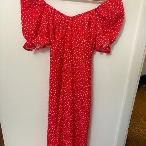 Röd prickig klänning med puffärmar - Superfin röd klänning med vita prickar och puffiga korta ärmar. Klänningen har resår vid axlarna och ett knytband i midjan för extra passform. Perfekt för sommarens alla tillfällen!