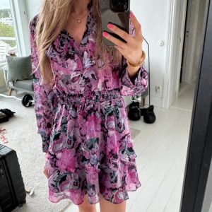Blommig rosa klänning från Zara - Supersöt kortklänning från Zara i rosa och lila toner med blommigt mönster. Klänningen har volangdetaljer, v-ringning och långa ärmar, samt resor i midjan!💓Aldrig använd