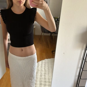 Svart ribbad topp med volangärmar från Zara - Säljer en svart ribbad topp från Zara med unika volangdetaljer på axlarna. Toppen är tight och croppad, perfekt att styla till både jeans och kjol. Är i storlek S men passar även XS. Materialet är mjukt och stretchigt för en bekväm passform.