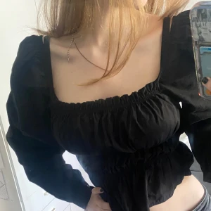 Svart blus med puffärmar från NA-KD - Säljer en svart snygg blus från NA-KD med långa puffärmar och smockad resår vid halsringning, midja och ärmslut. Säljer för att jag aldrig använder den tyvärr. 