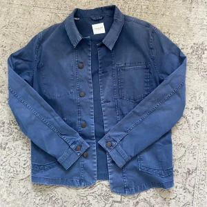Blå overshirt från Selected Homme - Säljer en blå overshirt från Selected Homme med tre stora fickor framtill och knappar längs hela framsidan. Riktig najs fade, hade använt den själv i vår/sommar men har växt ur den. 