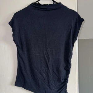 Mörkblå topp med rynkade detaljer - En enkel mörkblå topp med korta ärmar och snygga rynkade detaljer längs ena sidan. Andvänd ett fåtal gånger💕