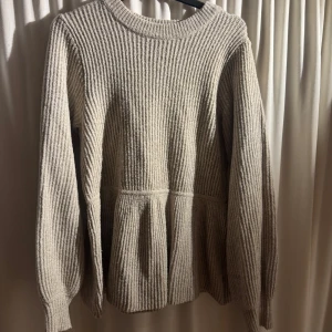 Beige stickad tröja från SAMSA Collection - Mysig beige stickad tröja från SAMSA Collection med ribbad struktur och rund hals. Den har en volang längst ne, sparsamt använd och super skön