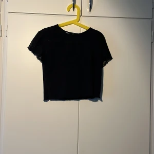 Svart croppad mesh-topp - Säljer en svart croppad topp i meshmaterial med korta ärmar. Toppen har en enkel rund halsringning och är lätt transparent. Perfekt att styla lager på lager eller till höga byxor.