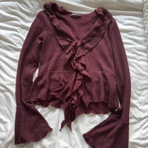 Vinröd volangtröja från Gina Tricot - Säljer en vinröd långärmad tröja från Gina Tricot med volangdetaljer längs fram och vid ärmslut. Använd ca 1-2 gånger så nästan helt ny!