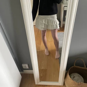 Vit volangkjol i jeans - Säljer en vit kort kjol i jeansmaterial med volanger och fransar nere vid kanten. Kjolen har klassiska jeansdetaljer som fickor och en knapp i midjan . Perfekt för dig som gillar en trendig och avslappnad stil. Passar perfekt till sommaren med en söt topp eller stickad tröja.