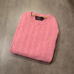 Rosa kabelstickad tröja från Morris Lady - Säljer en rosa kabelstickad tröja från Morris Lady i 100% pima bomull. Tröjan har rund halsringning, lång ärm och ett litet broderat emblem på bröstet. Perfekt för lager-på-lager under kyliga dagar. Tröjan är i bra skick men tagen vid halsen är lös på ett ställe som ni ser på bild 4. Bara att höra av sig vid funderingar!