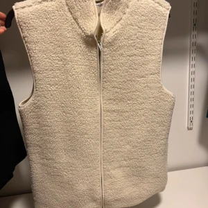 Beige fleeceväst med dragkedja - Mysig beige fleeceväst med hög krage och dragkedja framtill. Perfekt för lager-på-lager och enkel att matcha med olika outfits. Västen har en mjuk och fluffig yta som ger en avslappnad look.