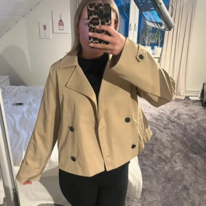 Beige kort trenchcoat från Vila - Säljer denna korta trenchcoat från vila som är slutsåld, har prislappar kvar och är helt ny