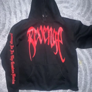 Svart hoodie från Revenge - Säljer en svart hoodie från Revenge med stor röd logga på bröstet och ett rött handavtryck på ryggen. Ärmen har röd text längs hela sidan. Priset går att diskutera vid snabbaffär