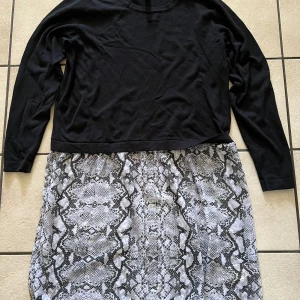 Svart långärmad klänning med ormmönstrad kjol från Rainbow - Säljer en snygg klänning från Rainbow med svart långärmad överdel och kjol i grått ormmönster. Perfekt för dig som vill sticka ut med en cool och trendig look. Bekväm passform och passar till många tillfällen.