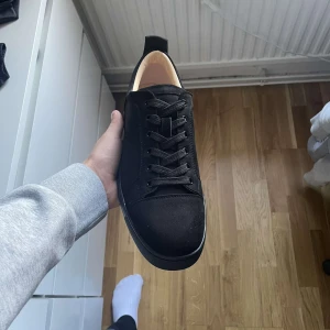 Svarta sneakers från Christian Louboutin - Säljer ett par svarta sneakers från Christian Louboutin med klassisk röd sula och snörning. Skorna har rund tå och är tillverkade i mocka med detaljer i skinn. Perfekta för dig som vill ha en stilren och lyxig look. Kvitto och certifikat finns. Vill nämligen bli av med dessa skor så snabbt som möjligt pga kronofogden 