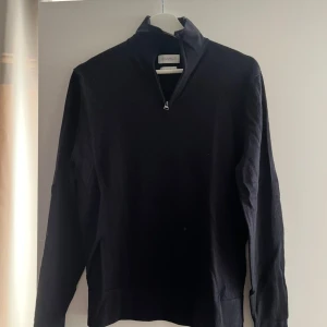 Mörkblå merinoullströja med halv dragkedja från These Glory Days - Mörkblå långärmad tröja i merinoull från These Glory Days. Tröjan har en halv dragkedja vid kragen och en stilren, enkel design. Perfekt för lager-på-lager och passar till många olika outfits.