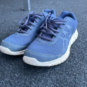 Blå sneakers med snörning - Säljer ett par blå sneakers med vit sula och snörning. Skorna har meshdetaljer på ovandelen för extra andningsförmåga och en sportig look. Perfekta för träning eller vardagsbruk.