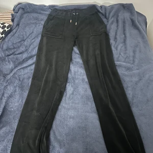 Svarta mjukisbyxor med fickor och broderad detalj - Svarta mjukisbyxor med bred resår och snörning i midjan. Byxorna har stora fickor fram och bak, samt en broderad bokstav på ena fickan. Mjukt och lent material som ger en avslappnad look.