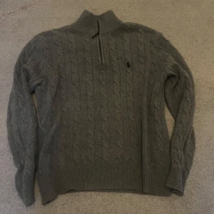 Grå kabelstickad tröja från Polo Ralph Lauren - Säljer en grå stickad tröja från Polo Ralph Lauren med halv dragkedja och hög krage. 