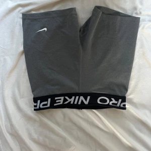 Grå Nike Pro shorts - Grå tighta Nike Pro shorts med svart resår i midjan där det står 'NIKE PRO' i vitt. Klassisk vit Nike-logga på ena benet. Perfekta för träning eller sport. Mjukt och stretchigt material som sitter skönt på kroppen.Skriv privat för fler bilder eller andra frågor 💞 perfekt för en cheerleading träning 