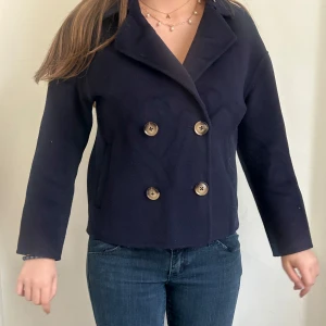 Mörkblå skepparkavaj med knappar - Säljer en klassisk mörkblå skepparkavaj med dubbelknäppning och bred krage. Jackan har långa ärmar och en stilren design som passar perfekt till jeans eller kjol. Enkel att matcha och ger en snygg look.