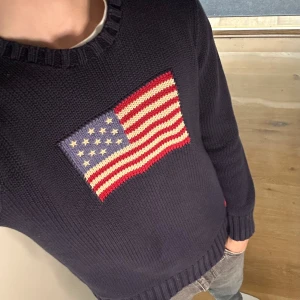 Ralph Lauren USA - Ralph Lauren stickad tröja i navy blått med den klassiska USA-flaggan. Märkt XL men sitter som M (jag är 180 cm, se bild). Äkta vara i fint skick. Hör av dig vid frågor! Kika gärna in min profil för fler trendiga plagg 😊