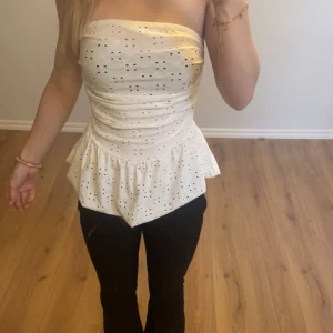 Vit söt bandå topp - Säljer en söt vit bandåtopp med blommönster och ”volang” nertill. Toppen har bra passform och säljer för att den inte lyckats komma till användning. Inga defekter förutom att lappen är borta💗