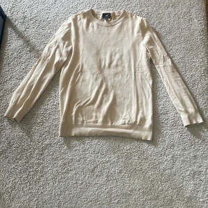 Beige tröja i bomull från H&M - Säljer en stilren beige långärmad tröja från H&M i slim fit-modell. Tröjan är tillverkad i mjuk bomull och har rund halsringning samt ribbade muddar vid ärmslut och nederkant. Perfekt för en enkel och clean look.