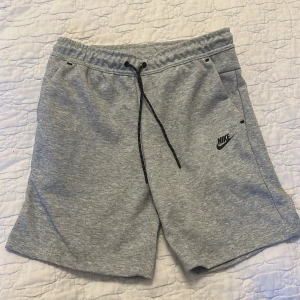 Grå shorts från Nike med snörning - Snygga grå shorts från Nike med svart snörning i midjan och diskret Nike-logga på ena benet. Shortsen har sidofickor och en bakficka med dragkedja. Perfekta för en avslappnad stil. Aldrig använda har bara legat i garderoben men är i perfekt skick, shortsen är i storlek L men kan användas av personer som bär både M och L. Jag kan diskutera priset