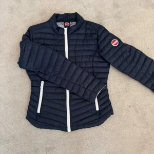 Mörkblå quiltad dunjacka från Colmar - Säljer en mörkblå quiltad dunjacka från Colmar med vita dragkedjor och rund krage. Jackan är sparsamt använd och i bra skick! Kemtvättad.                         Perfekt för kyliga dagar. Storlek 12 år. Köpt på Lucca i Stockholm. 