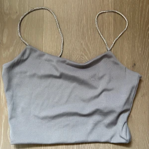 Ljusgrå linnetopp med glittriga axelband - Säljer en ljusgrå linnetopp från FB Sister i storlek M. Toppen har tunna, glittriga axelband och en enkel, stilren design. 