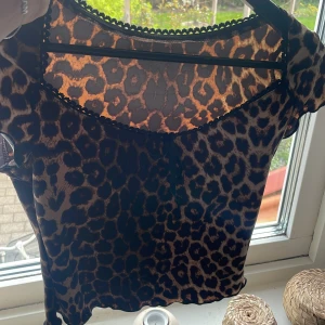 Leopardmönstrad topp - Säljer en kortärmad topp i leopardmönster. Toppen har rund halsringning med dekorativ kant och är figurnära i modellen. Perfekt för dig som gillar djurmönster och vill sticka ut åt de bra hållet