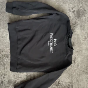 Svart sweatshirt från Peak Performance - Svart sweatshirt från Peak Performance med vit logotyp på bröstet. Klassisk rund halsringning och långa ärmar. Perfekt för en avslappnad och sportig stil.