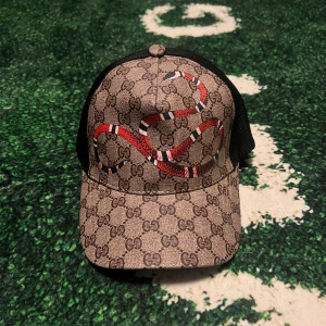  Keps med orm och GG-mönster - Snygg keps med klassiskt GG-mönster i beige och brunt, prydd med en röd, svart och vit orm på framsidan. Baksidan är i svart mesh. Justerbar rem baktill. Vid mer funderingar skriv!!! Vid snabb affär bättre pris.