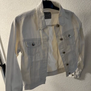 Vit jeansjacka från Denim & CO - Säljer en klassisk vit jeansjacka från Denim & CO. Jackan har två bröstfickor med knappar, krage och knappstängning framtill. Perfekt att slänga över en t-shirt eller klänning för en fräsch look.