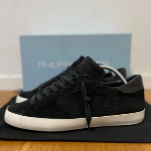 Svarta sneakers från Philippe Model - Snygga svarta sneakers från Philippe Model i mocka med vit platt sula. Skorna har snörning och en diskret logga på sidan. Perfekta för en stilren och avslappnad look. Storlek 43. Bra skick! Skriv för frågor! Nypris runt 3000 kr