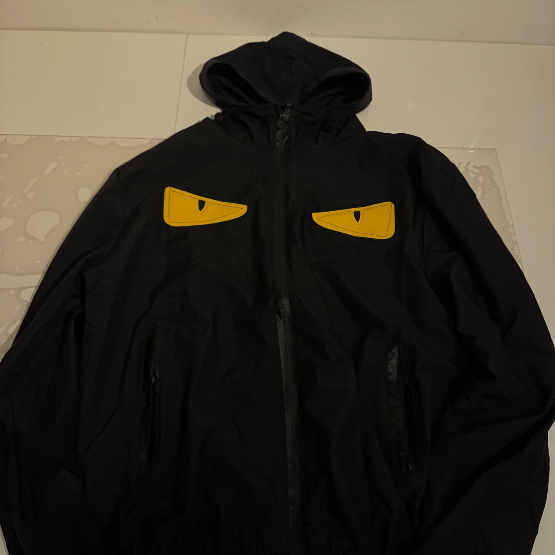 Svart vindjacka med gula ögon-detaljer