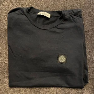 Mörkblå Stone Island T-shirt  - Säljer en mörkblå t-shirt från Stone Island Junior med klassisk rund hals och broderad logotyp på bröstet. Modellen är 170cm lång. Är upp för förhandling. Hesitera inte att fråga något.