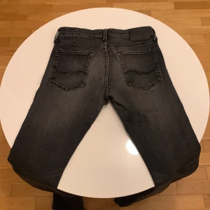 Svarta jeans från Jack & Jones - Säljer ett par svarta jeans från Jack & Jones med klassisk femficksdesign och svarta sömmar. Jeansen har normal passform och raka ben. Perfekta för dig som gillar en stilren look.