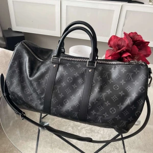 Keepall 55 väska - Oanvänd Keepall 55 med svart läder och silvrig dragkedja. Axelband, lås och nyckel samt dustbag och diverse detaljer medföljer, priset är inte hugget i sten