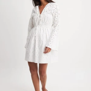 Vit klänning från NA-KD  till student eller avslutning - Vit, långärmad klänning från NA-KD  i ”anglaise”-tyg, alltså med ett genombrutet hålmönster. Somrigt och fint! Raka, långa ärmar, något vidare nedtill. Klänningen är mini- till halvkort, beroende på kroppsbyggnad. Dragsko i båda bystsömmarna gör överdelen anpassningsbar i hur vid/tajt den behöver vara. Klänningen köptes förra året och är endast använd en gång, till avslutning. Fläckfri och hel.