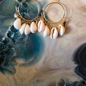 Guldiga örhängen med snäckor -  Handgjorda örhängen med snäckskal Vackra örhängen med guldfärgade ringar och naturliga snäckskal.  Bekväma att bära, perfekta för sommarens alla tillfällen. Ett stilrent smycke med en touch av havets charm. 